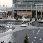 Vista di Piazza Gae Aulenti a Milano, luogo dove una donna di 43 anni è stata accoltellata alle spalle. L’immagine mostra l’area moderna con fontane e passanti.