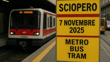 Cartello giallo con la scritta “Sciopero 7 novembre 2025 metro bus tram” alla stazione di Milano, con treno e tram ATM fermi sullo sfondo.